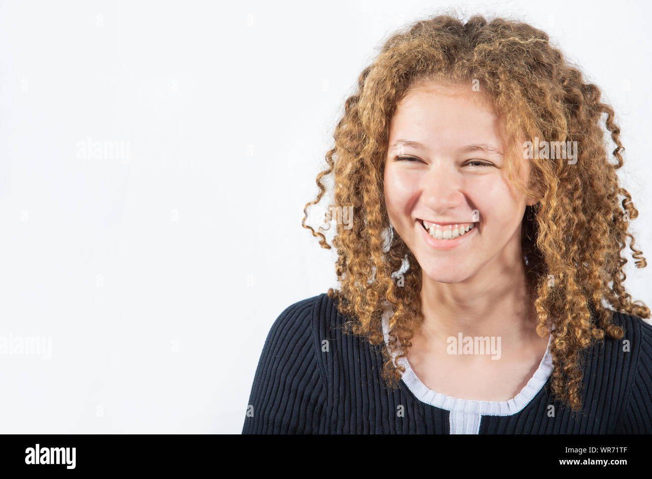 Smiling happy teenage girl with curly hair looking to camera over grey ...