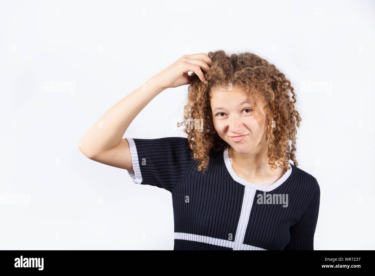 Confused young girl scratching her head looking frustrated over white