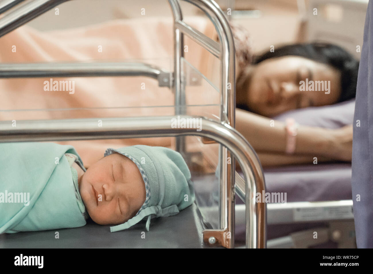 Newborn baby laying in crib with his mother lying on bed side Stock Photo
