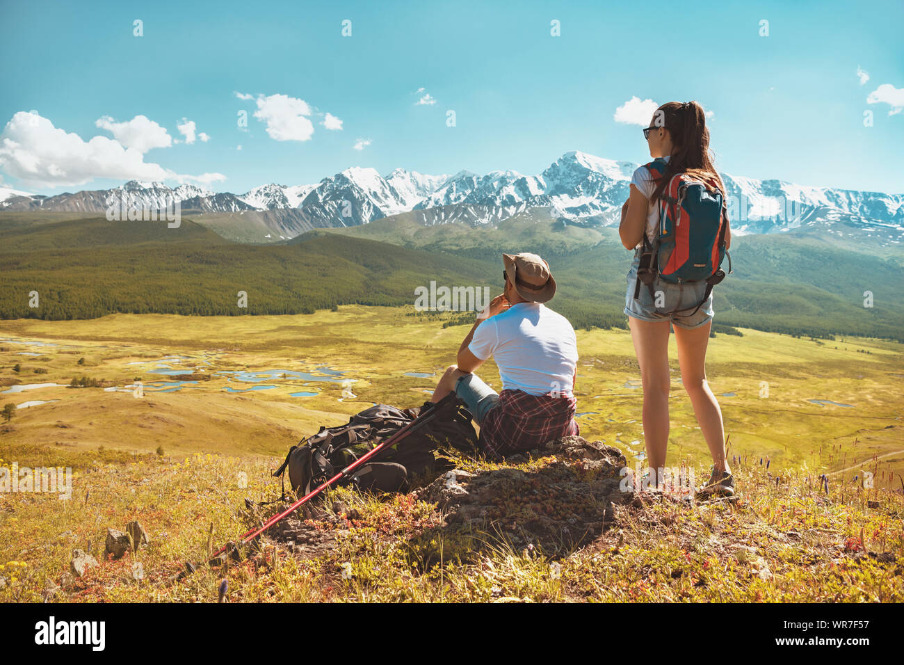 Two hikers relaxing on hill top and looks at white mountains Stock ...
