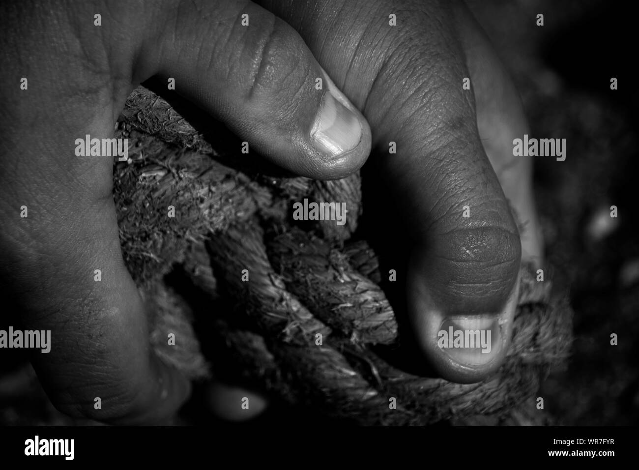 A close up of a mans hands holding thick worn old rope in black and white Stock Photo