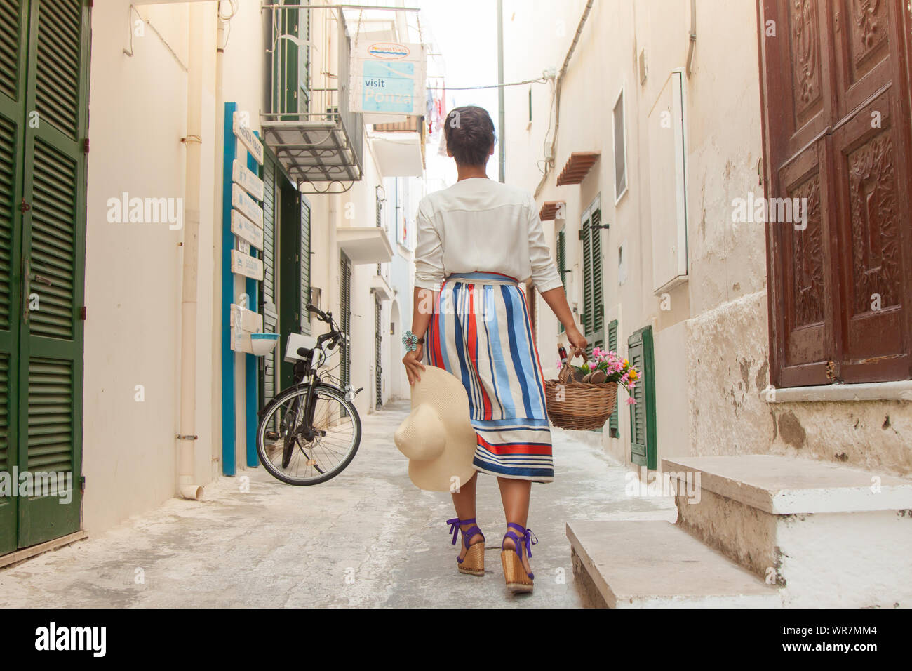 Young woman walking in a typical alley on Ponza island town, Italy. Fashion dress and sunglasses, white building. Stock Photo