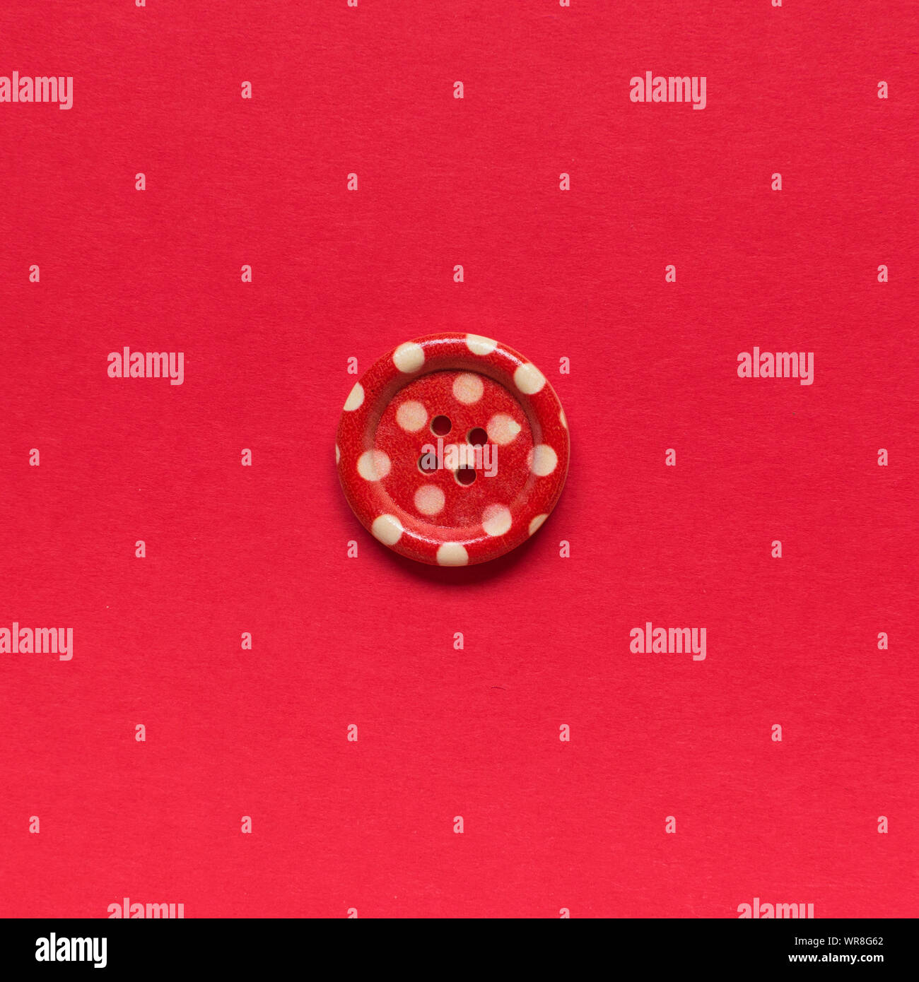 Single red sewing button with white dots on red background. Stock Photo