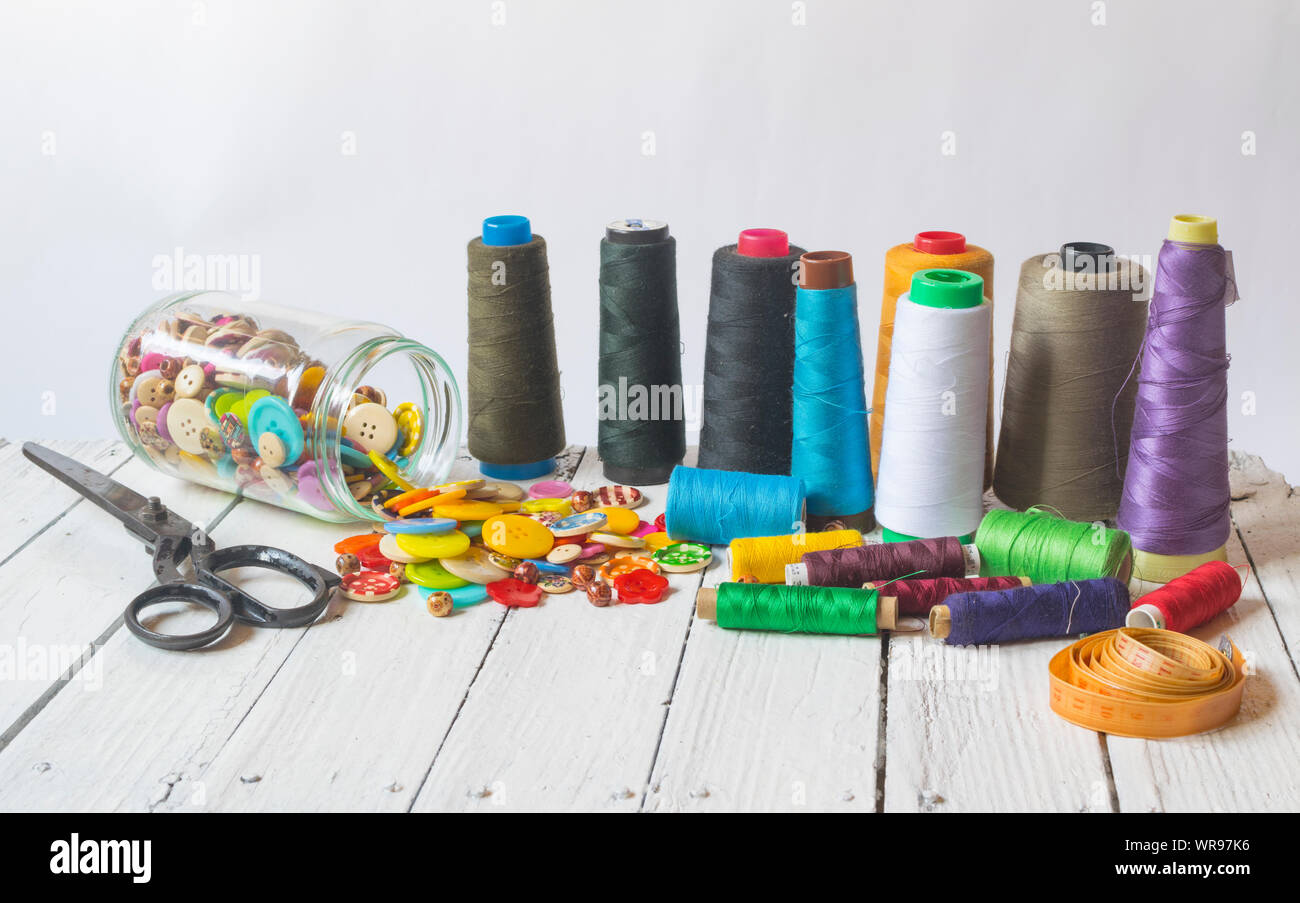 Sewing material (sewing buttons ,sccissors , threads) on old white table with white background Stock Photo
