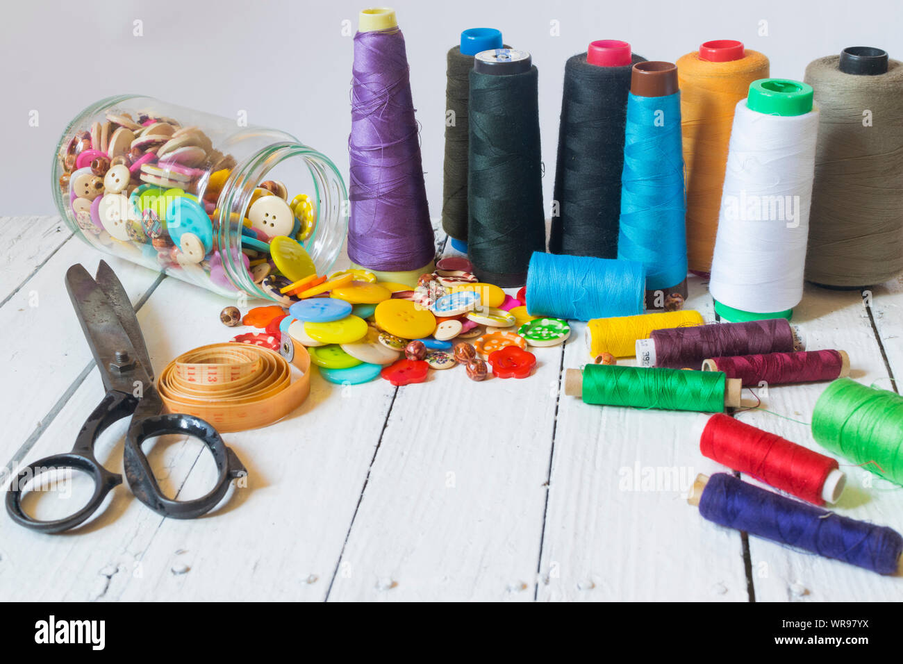 Sewing material (sewing buttons ,sccissors , threads) on old white table with white background Stock Photo