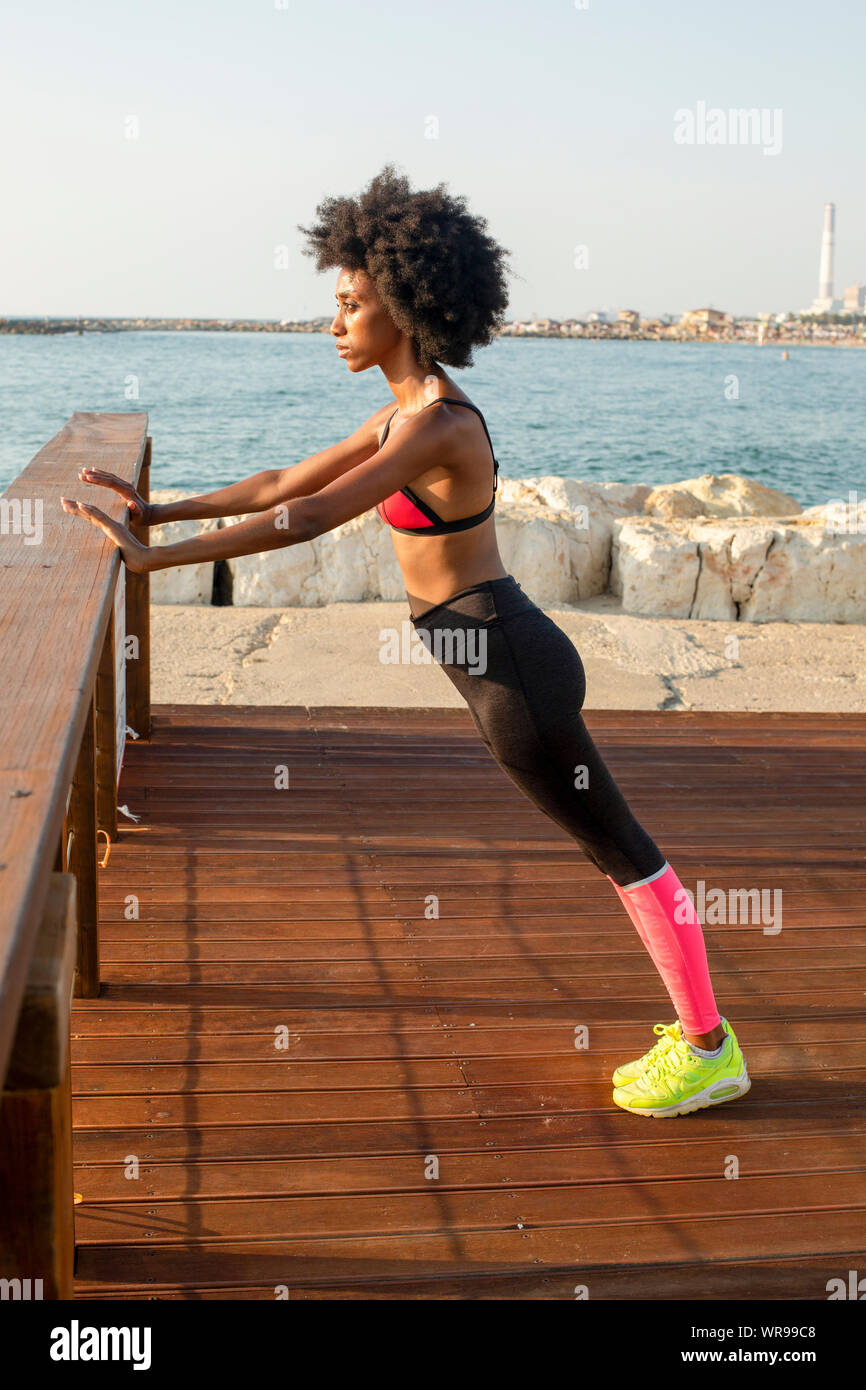 happy young african woman stretching and warming up before an outdoor workout. The Mediterranean sea in the background Stock Photo