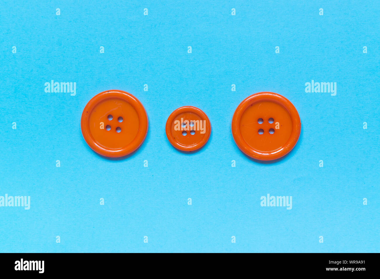 Three Various orange sewing buttons on blue background. Stock Photo