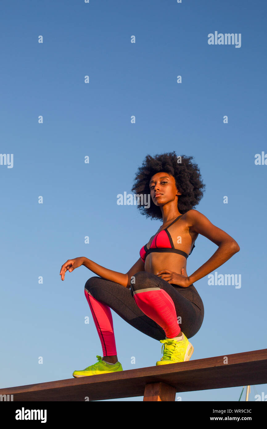 happy young african woman stretching and warming up before an outdoor workout. with a beautiful blue sky background Stock Photo