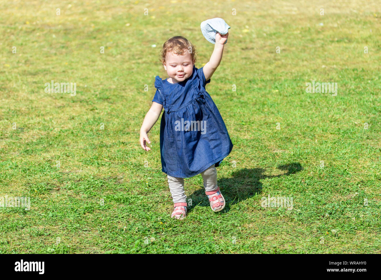 Little Baby Girl Runs Across The Field In A Denim Dress With A Panama In Her Hands Walking With A Child A Cheerful Little Girl Learning To Walk Stock Photo Alamy