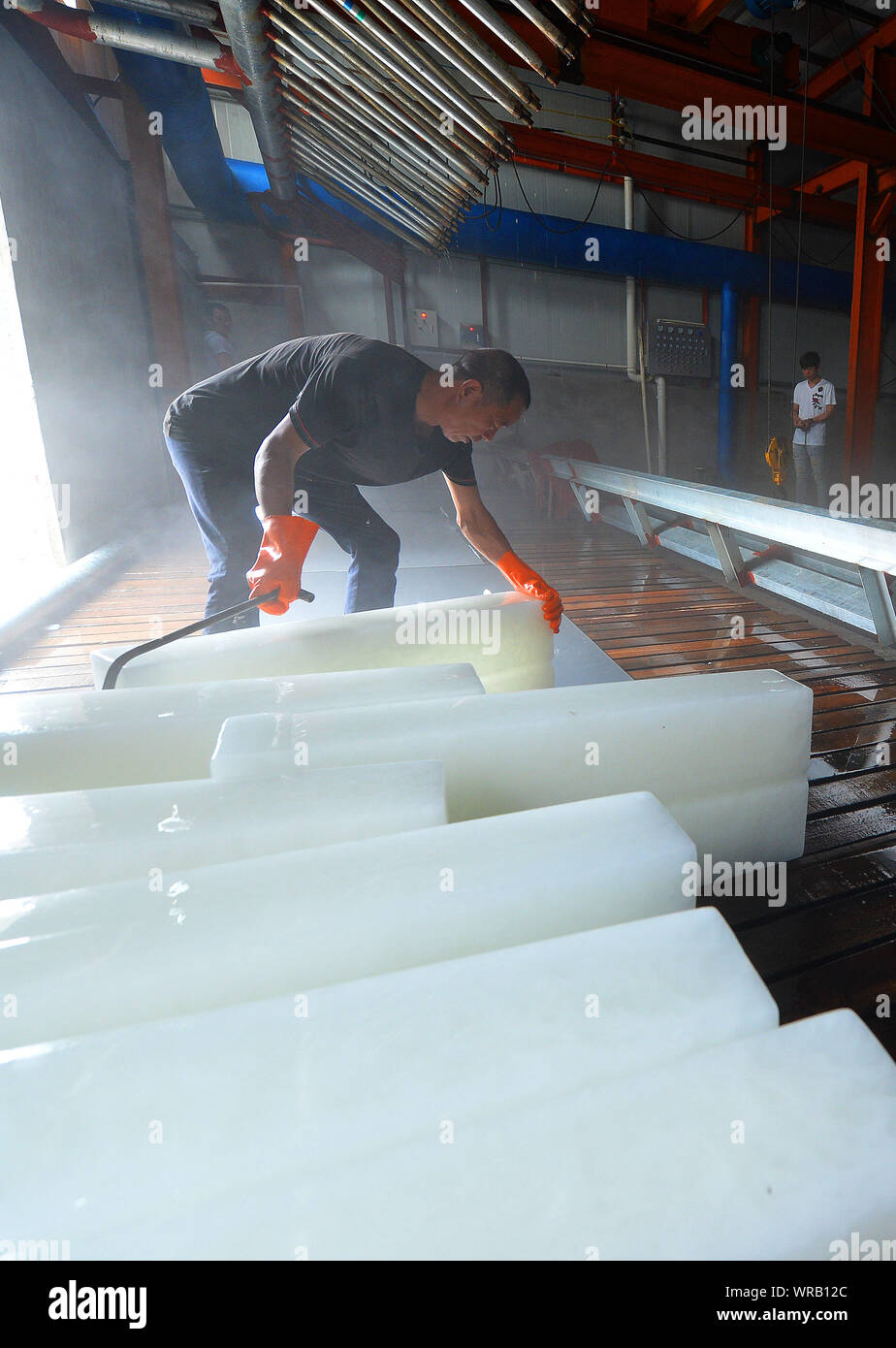 A Chinese worker moves newly-manufactured ice blocks at an ice factory on a scorcher in Liuhe Town, Taicang City, east China's Jiangsu Province, July Stock Photo