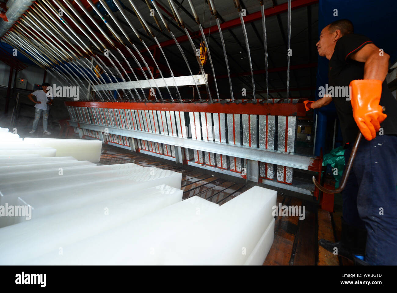 A Chinese worker watches water being poured into freezers next to newly-manufactured ice blocks at an ice factory on a scorcher in Liuhe Town, Taicang Stock Photo