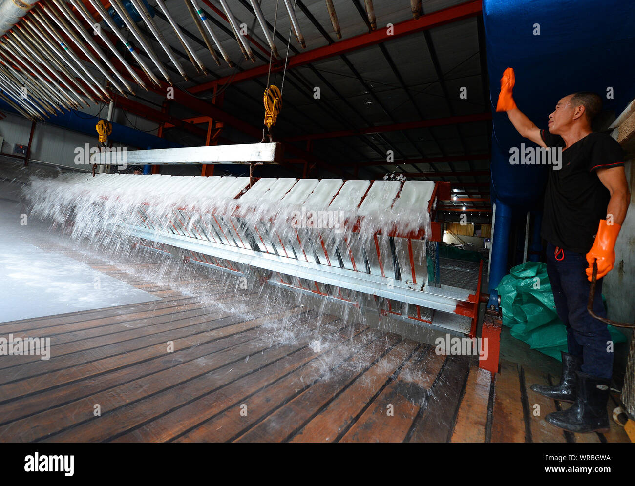 A Chinese worker directs another to unload newly-manufactured ice blocks at an ice factory on a scorcher in Liuhe Town, Taicang City, east China's Jia Stock Photo