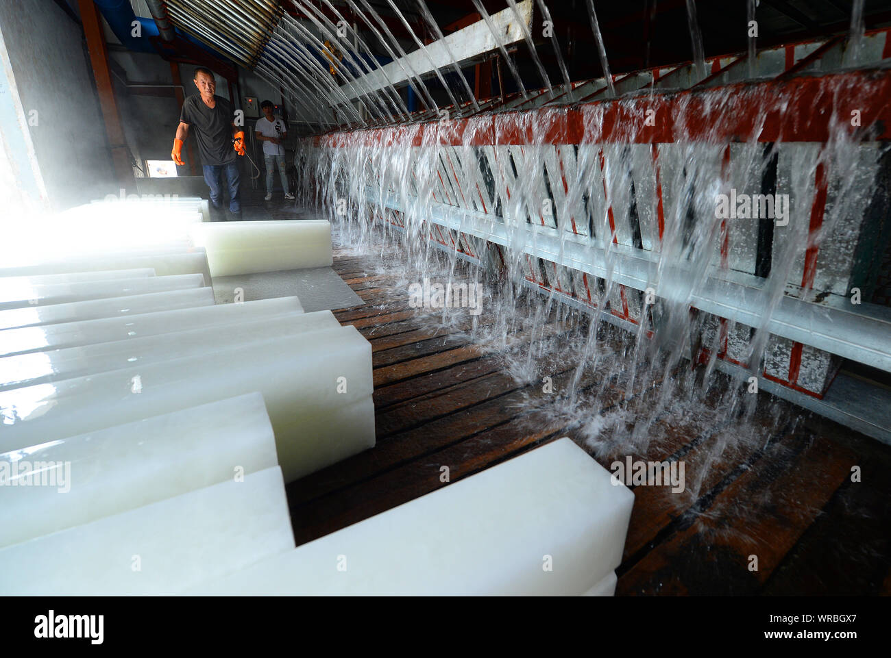 A Chinese worker moves newly-manufactured ice blocks as water is poured into freezers at an ice factory on a scorcher in Liuhe Town, Taicang City, eas Stock Photo
