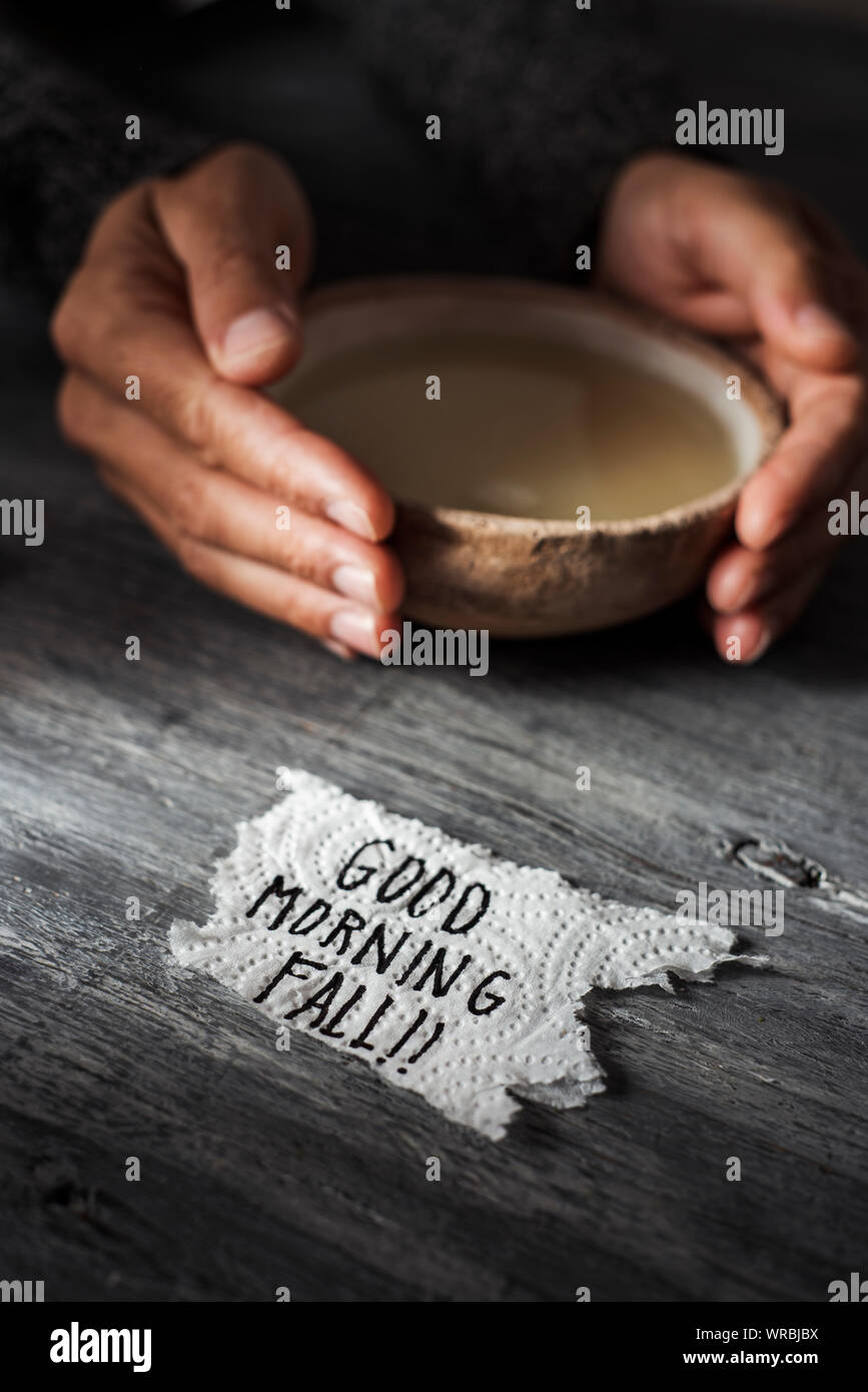 clouseup of a piece of paper with the text good morning fall on a gray rustic wooden table and a young caucasian man warming up with a bowl of hot sou Stock Photo