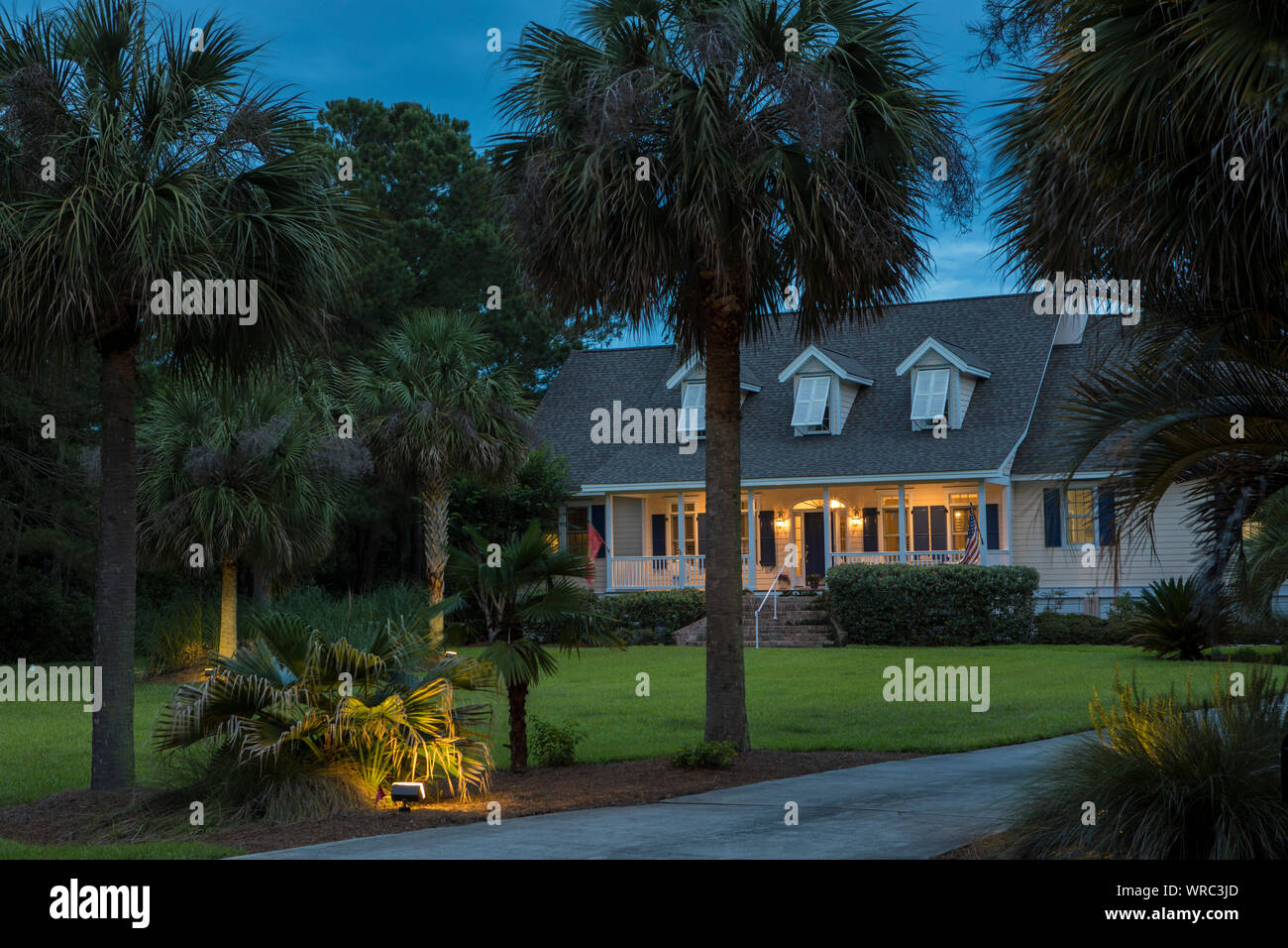 Beautiful cape cod house lit up at twilight with palm trees Stock Photo