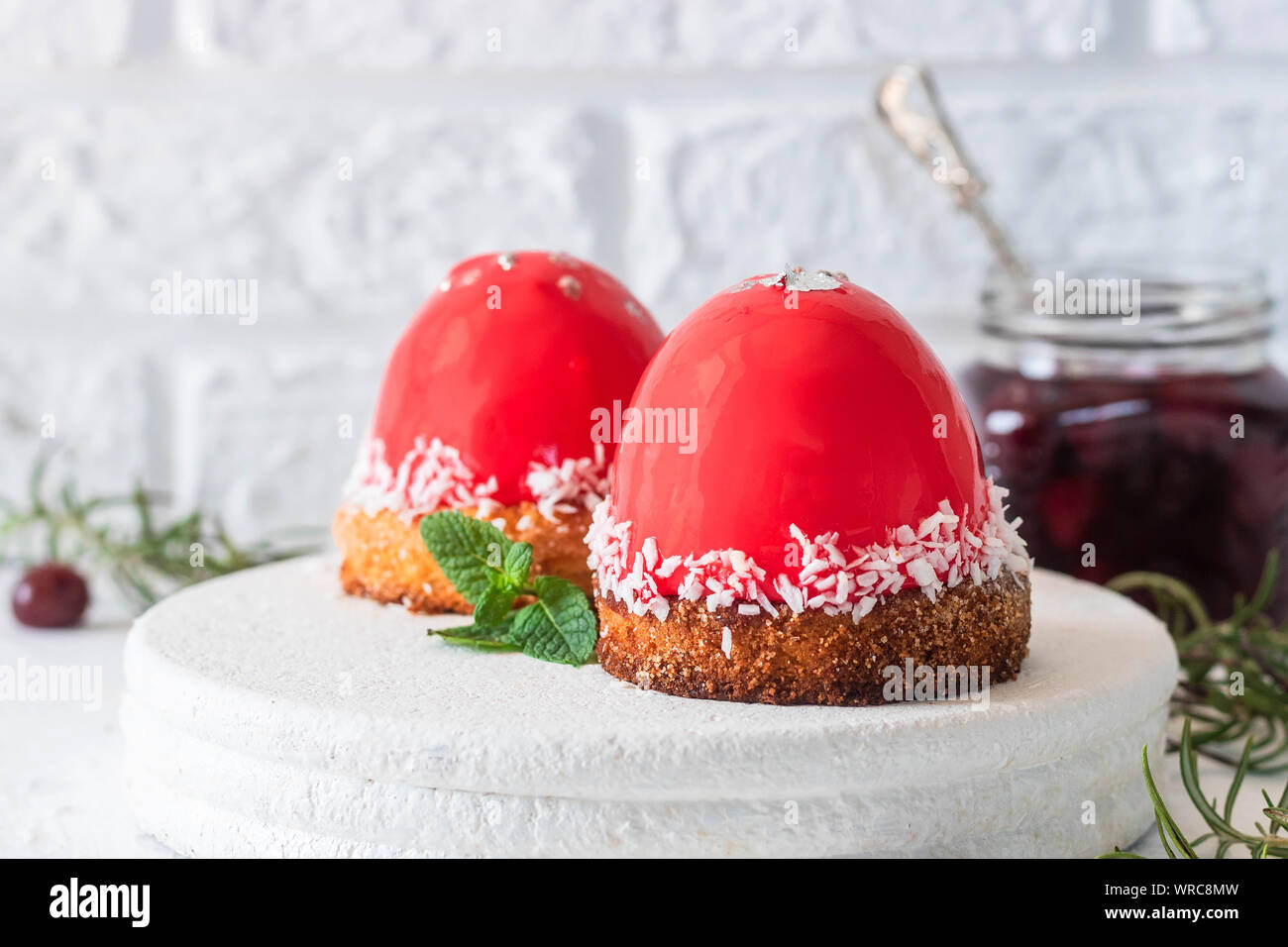 Fashionable mousse cake with mirror glaze and cherry filling on a pillow of coconut cookies with coconut flakes. Modern dessert. Stock Photo