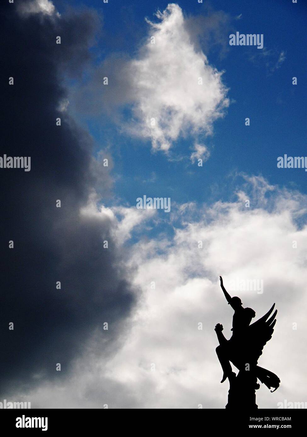 Statue Of Fallen Angel Against Cloudy Sky Stock Photo