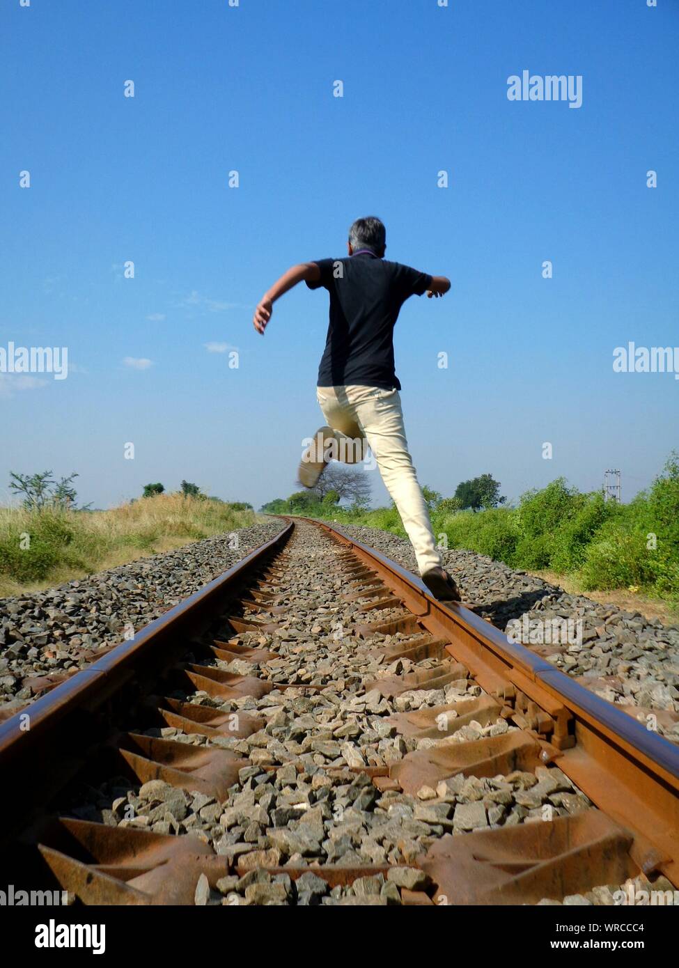 Full Length Rear View Of Man Jumping Over Railroad Track Stock Photo