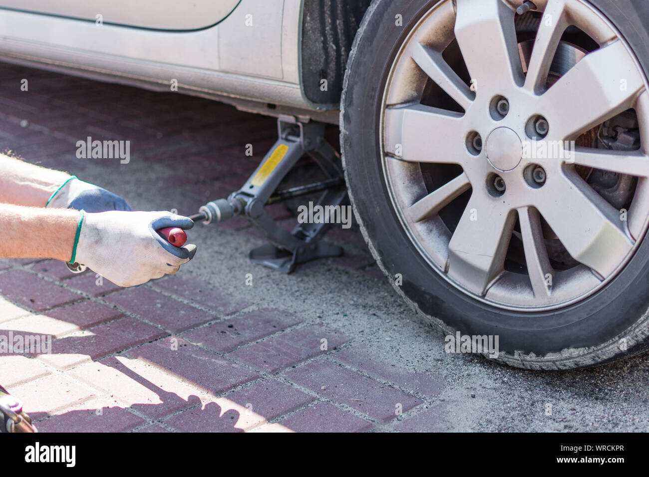 Mechanic changing wheel on car with a wrench outdoor in a sunny day