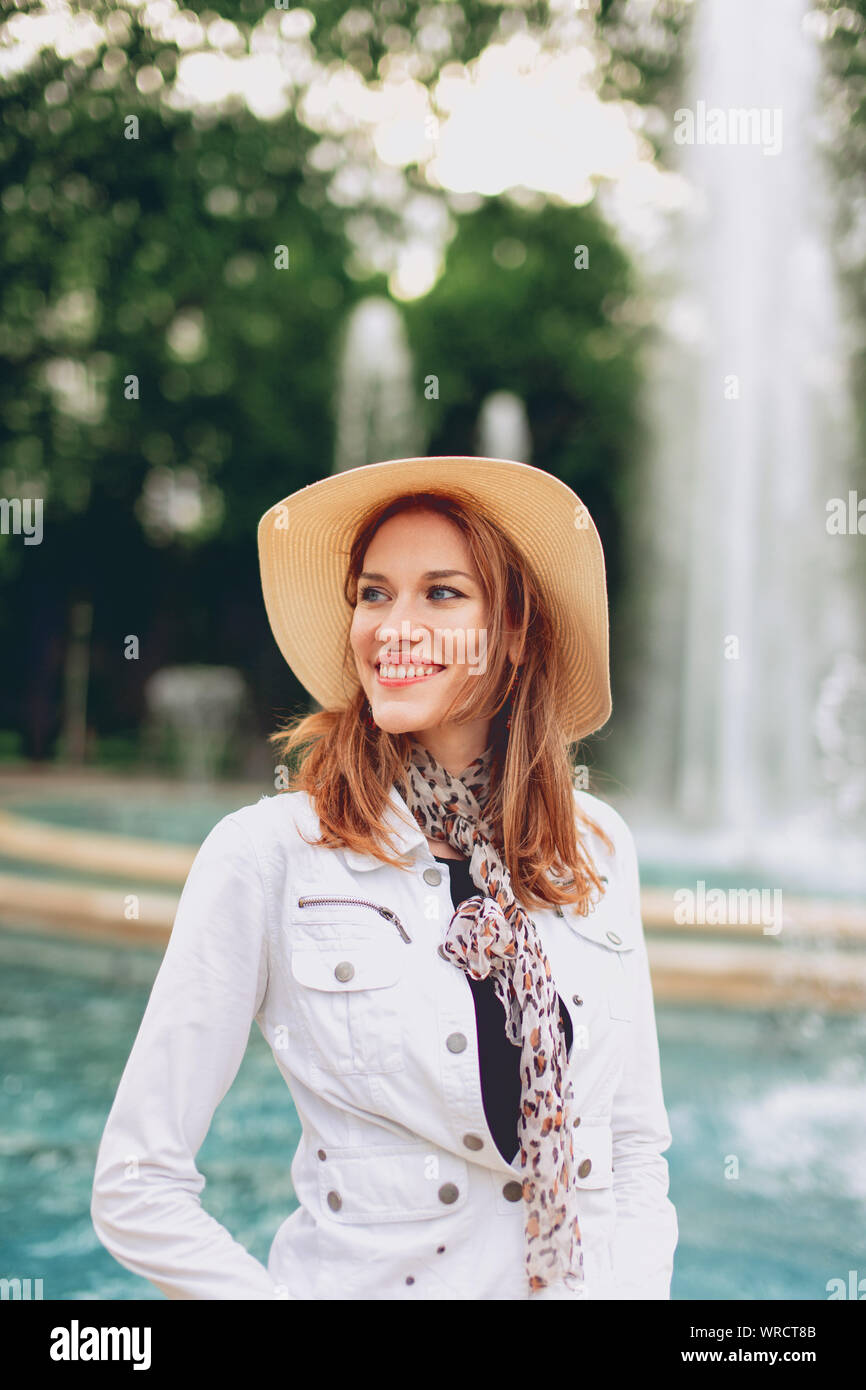 Happy young stylish woman smiling in park with fountain at autumn Stock Photo