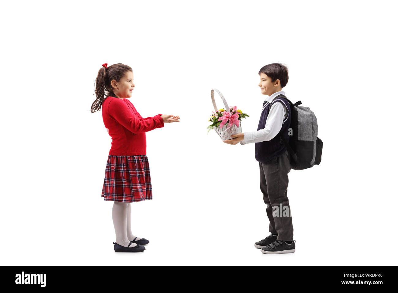 Full length profile shot of a schoolboy giving a basket with flowers to a little girl isolated on white background Stock Photo