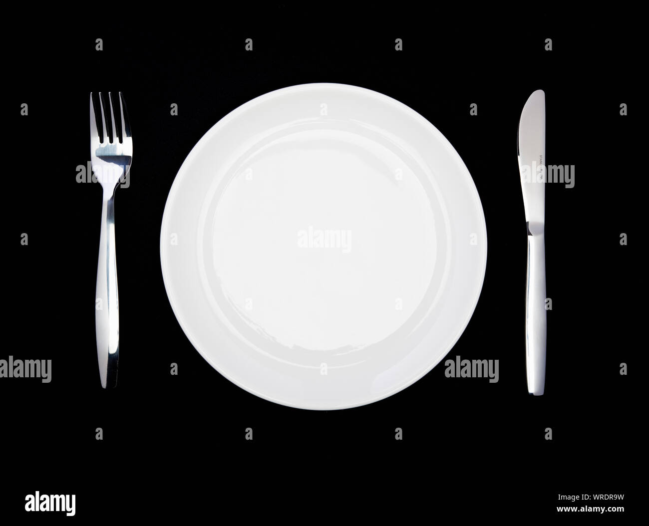 Place setting, white plate, knife and fork, from above on a black background Stock Photo