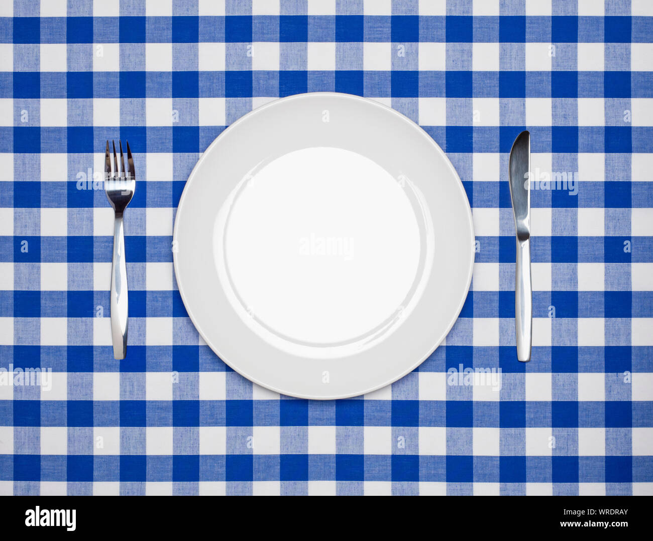 Place setting, round white plate, knife and fork, from above on a blue gingham tablecloth Stock Photo