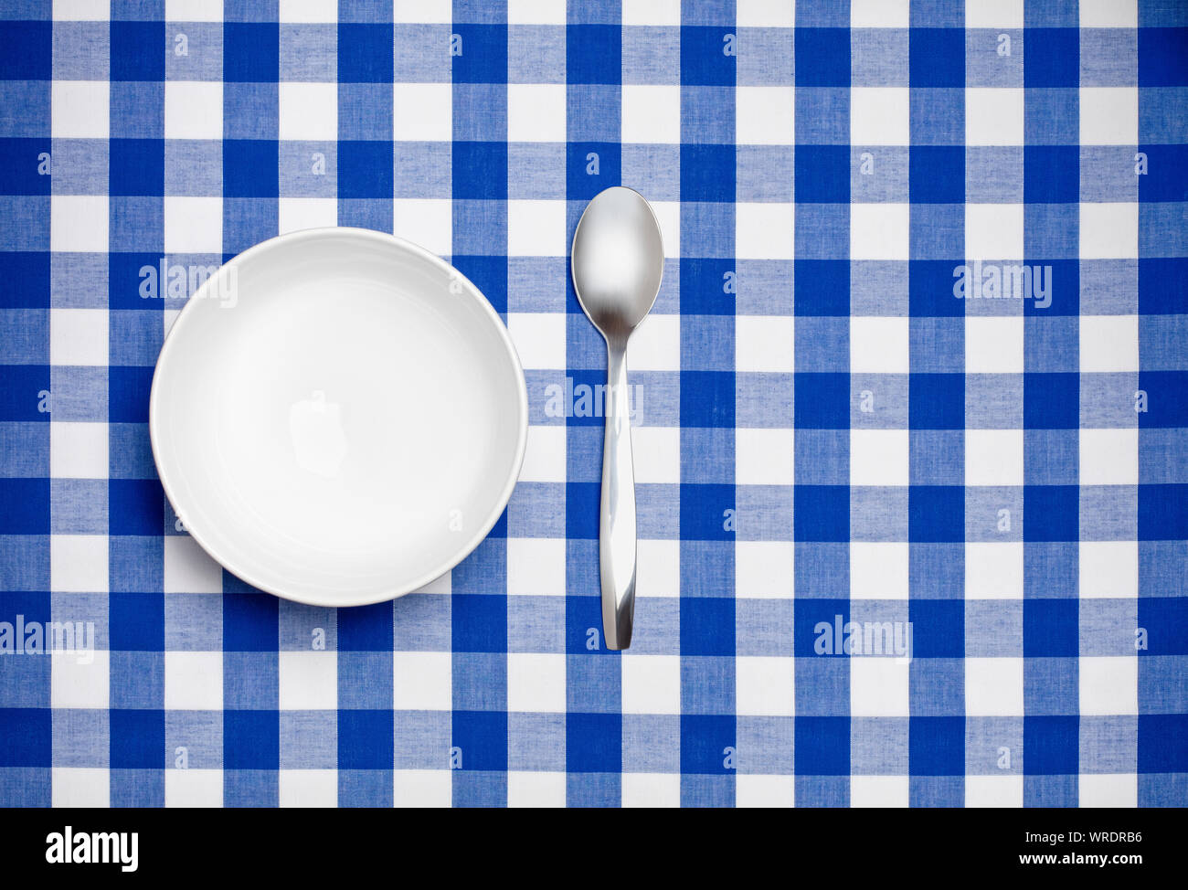 Empty white bowl and spoon on a blue gingham tablecloth Stock Photo