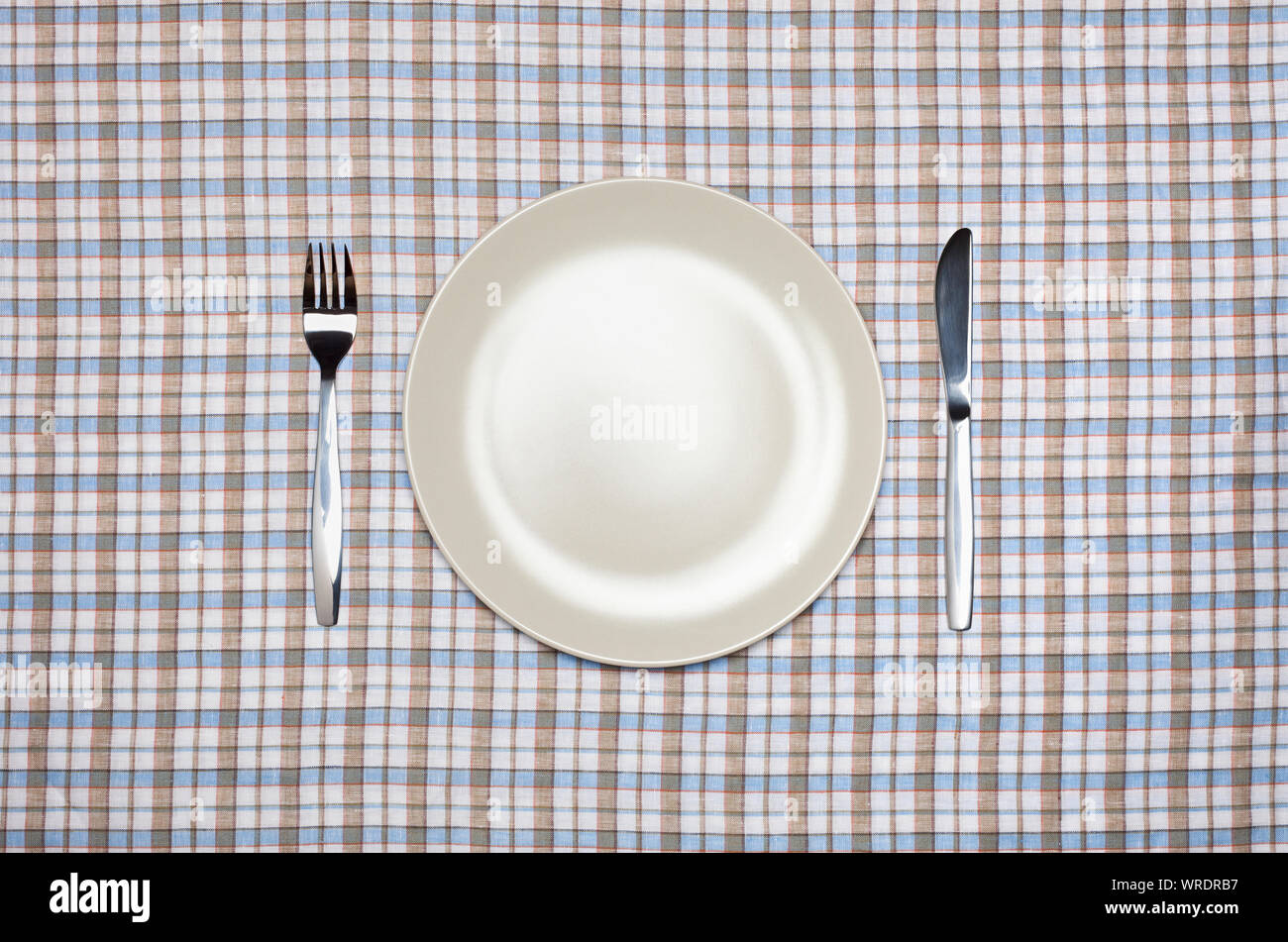 Place setting, white plate, knife and fork, from above on a pastel check tablecloth Stock Photo