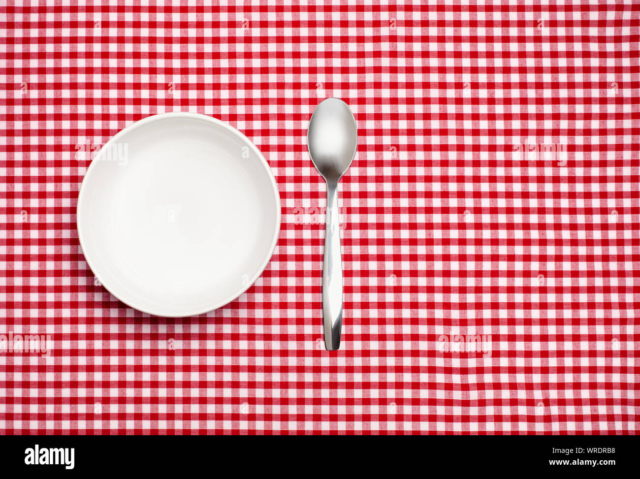 Empty white bowl and spoon on a red gingham tablecloth Stock Photo