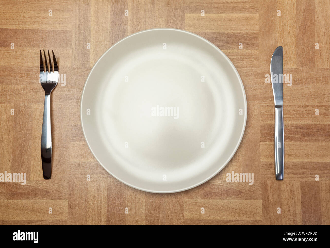 Place setting, white plate, knife and fork, from above on a wooden tabletop Stock Photo