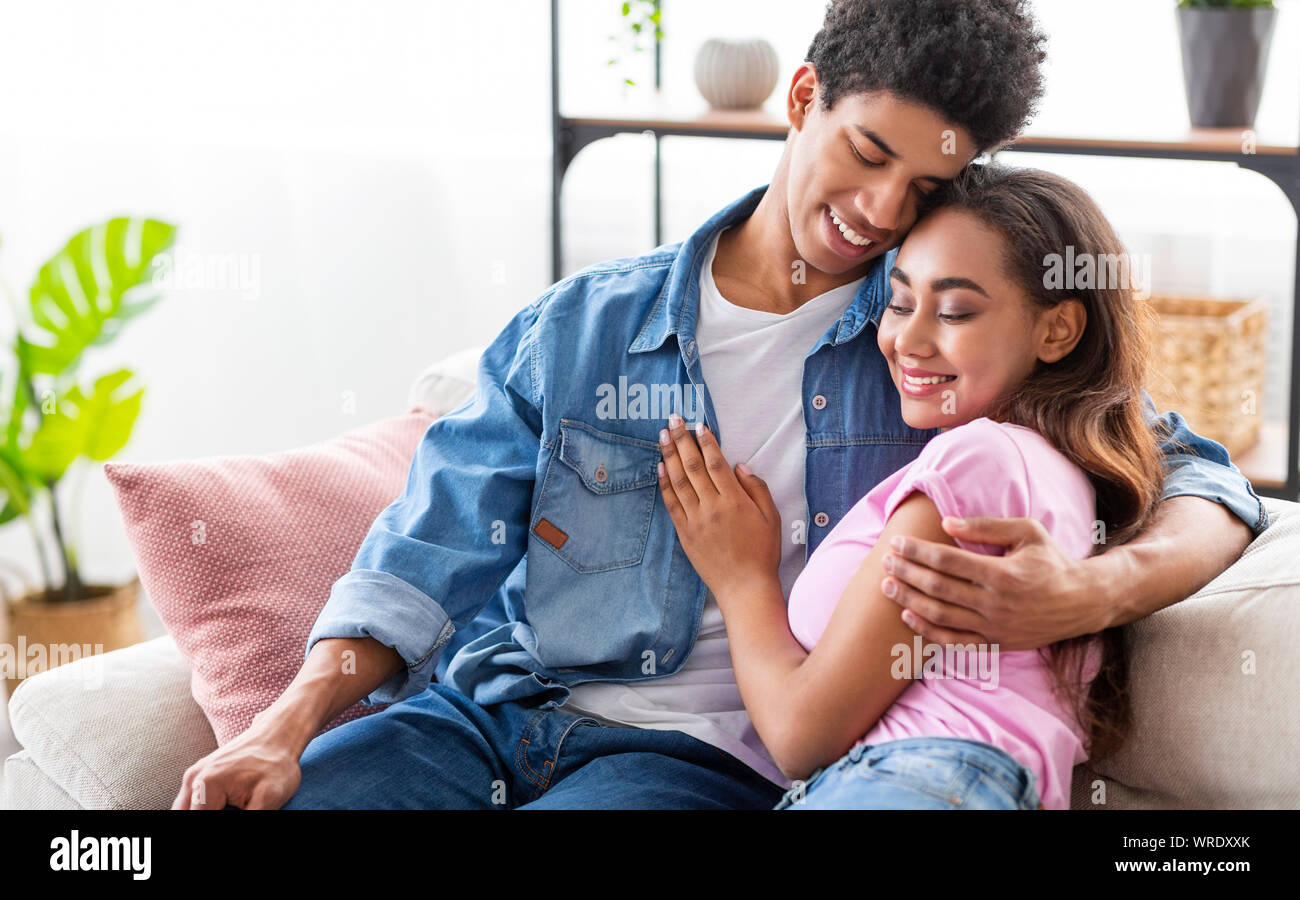 Young people sitting on couch at home, cuddling each other Stock Photo