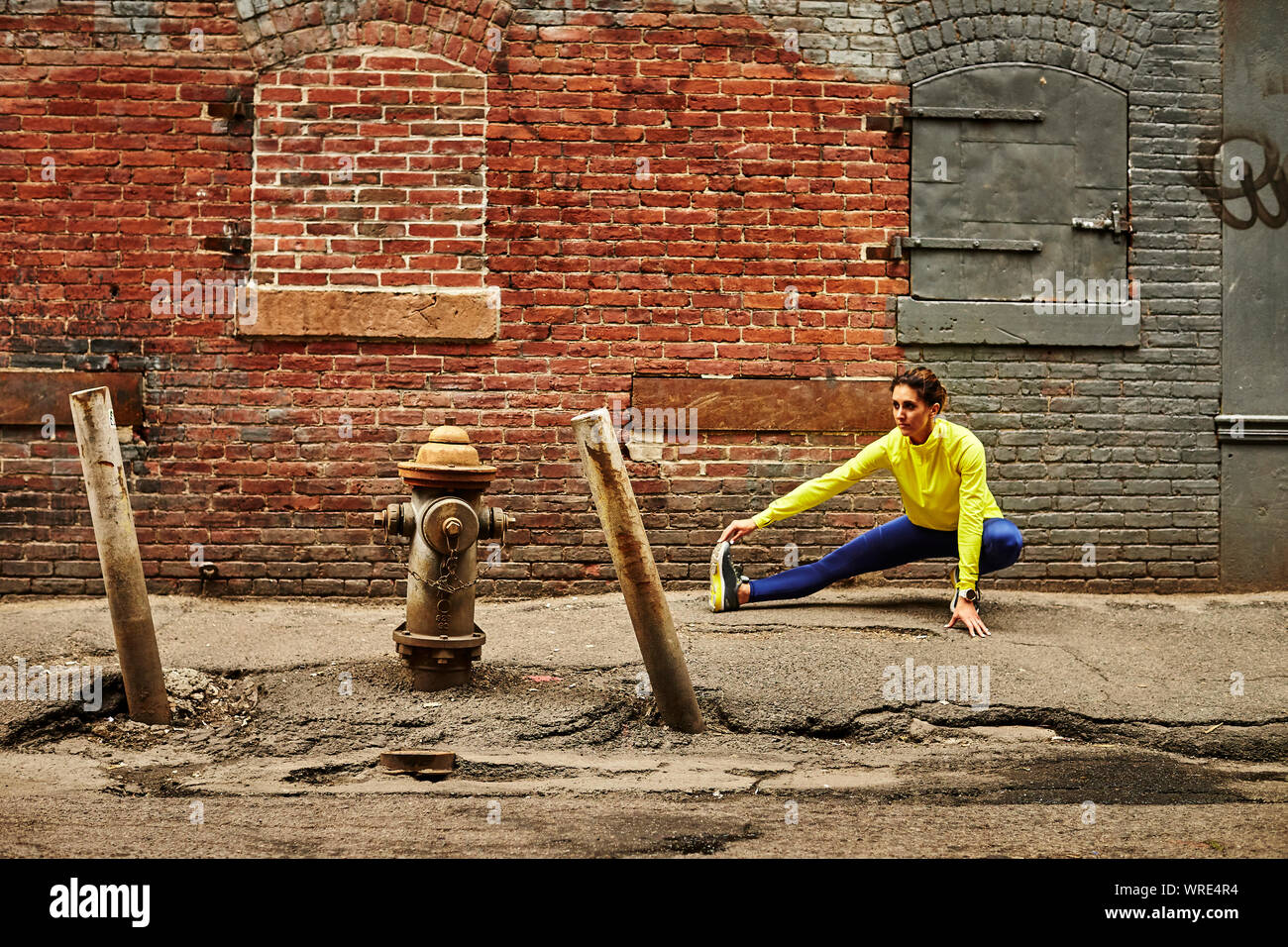 A female runner stretching on a gritty urban street. Stock Photo