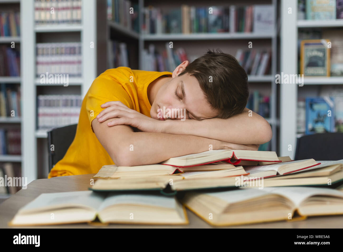 Tired young guy napping on books in library Stock Photo - Alamy