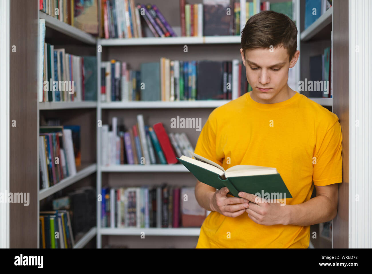 Smart male student reading book between bookshelves Stock Photo