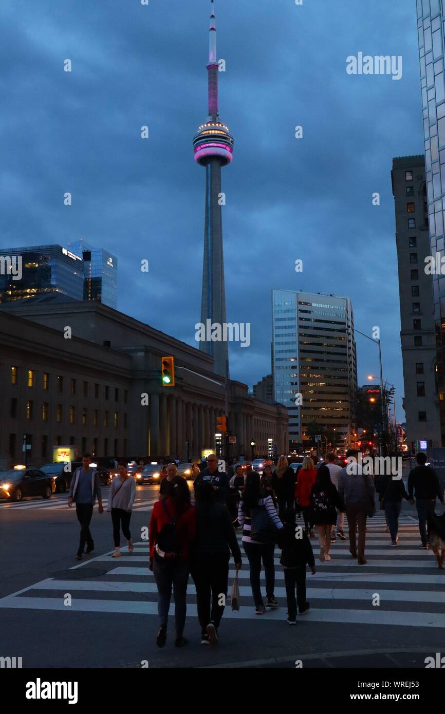 People cross a night street in Toronto with a brightly lit CN Tower in the background Stock Photo