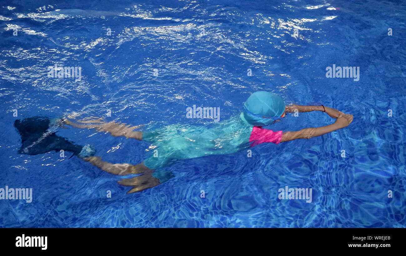 Cute little girl is lerning to swim in swimming pool in slow motion. She is in swimsuit, cap and