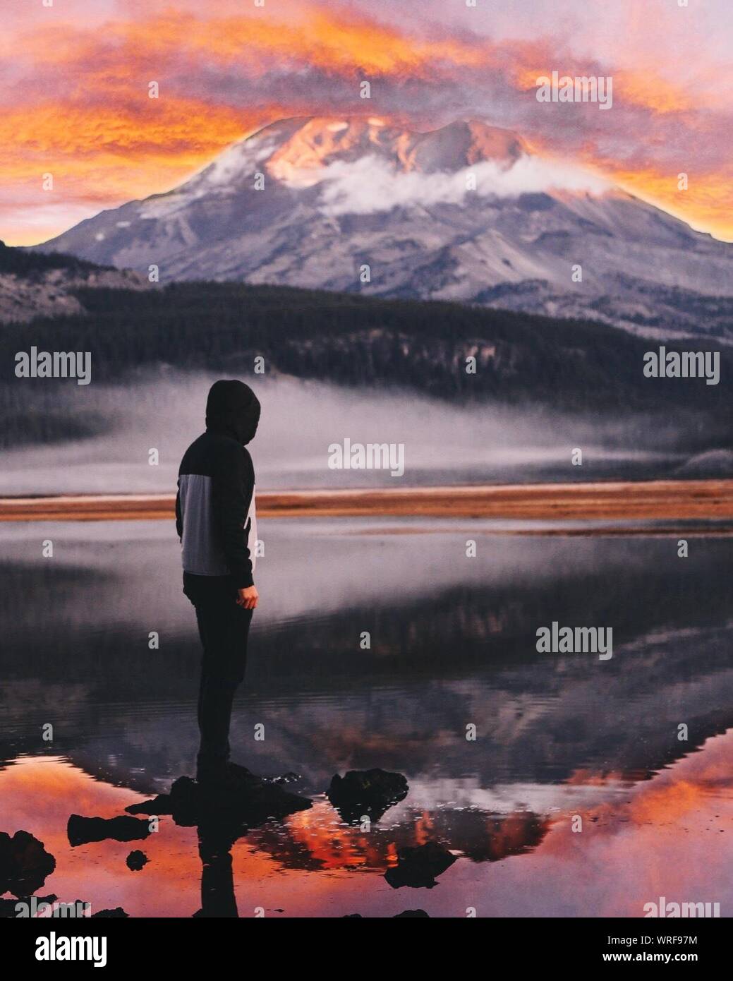 Man Standing On Rock In Sparks Lake Against Mountain During Sunset Stock Photo