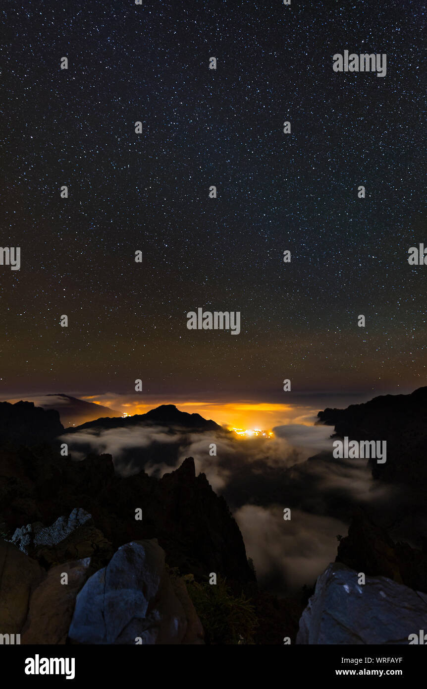 Starscape above the Caldera de Taburiente in La Palma, Spain with illuminated villages below the clouds. Stock Photo