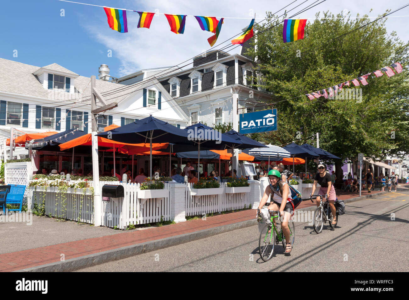Bicycle riders pass Patio American Grill restaurant on Commercial Street in Provincetown, Massachusetts. Stock Photo