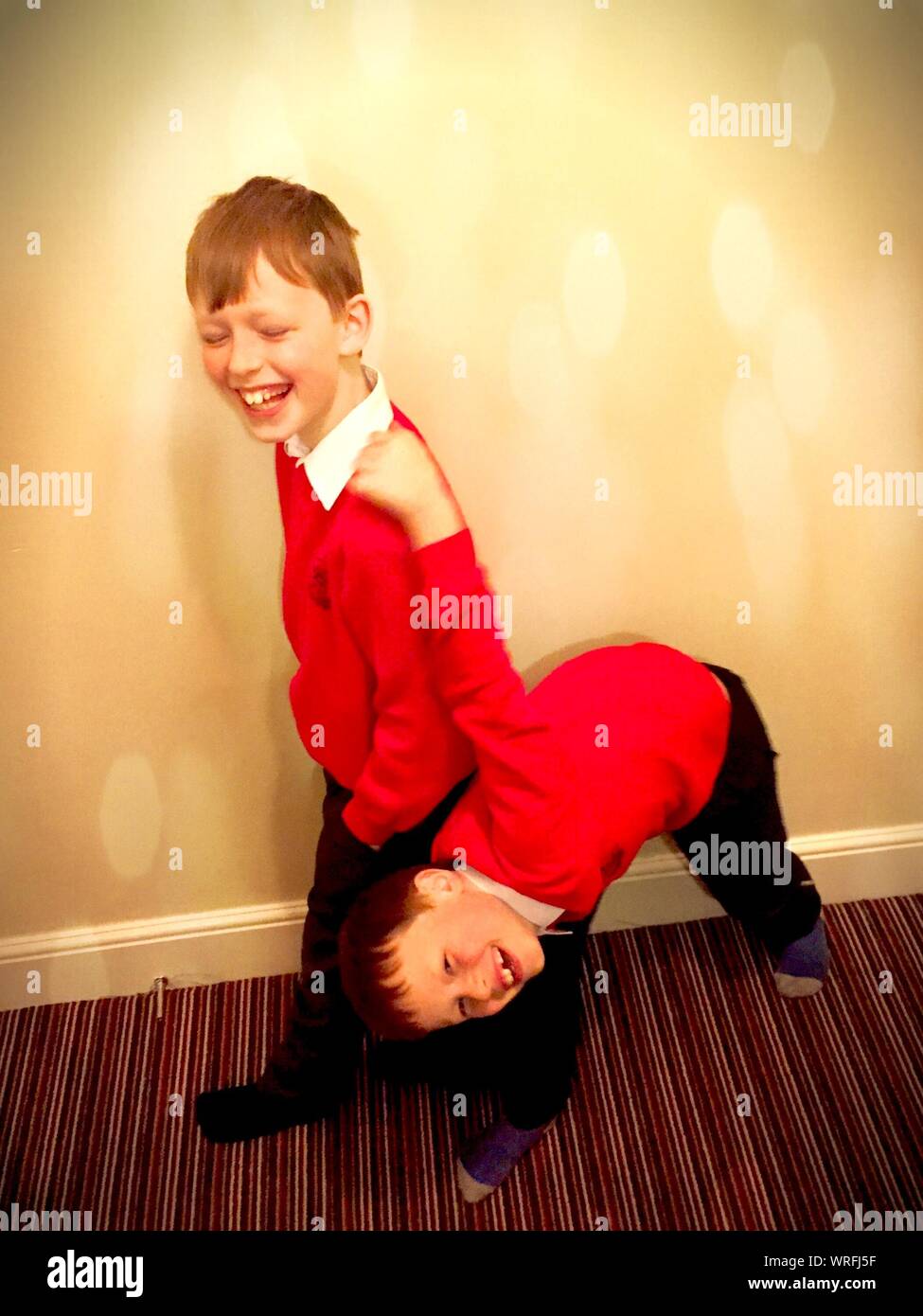 Happy Brothers Wearing School Uniforms Against Wall At Home Stock Photo