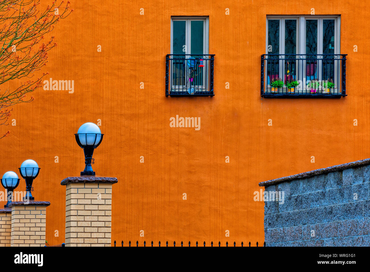 Abstract look of the side of a building with flower pots in window.  A row of brick post with lights on top and the top of an iron fencing. Stock Photo