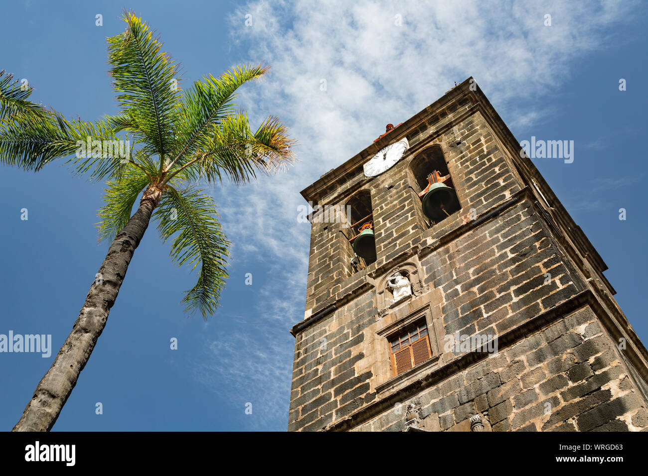 The tower of the church Iglesia Matriz de El Salvador with a palm tree and blue sky in Santa Cruz de La Palma, Spain. Stock Photo