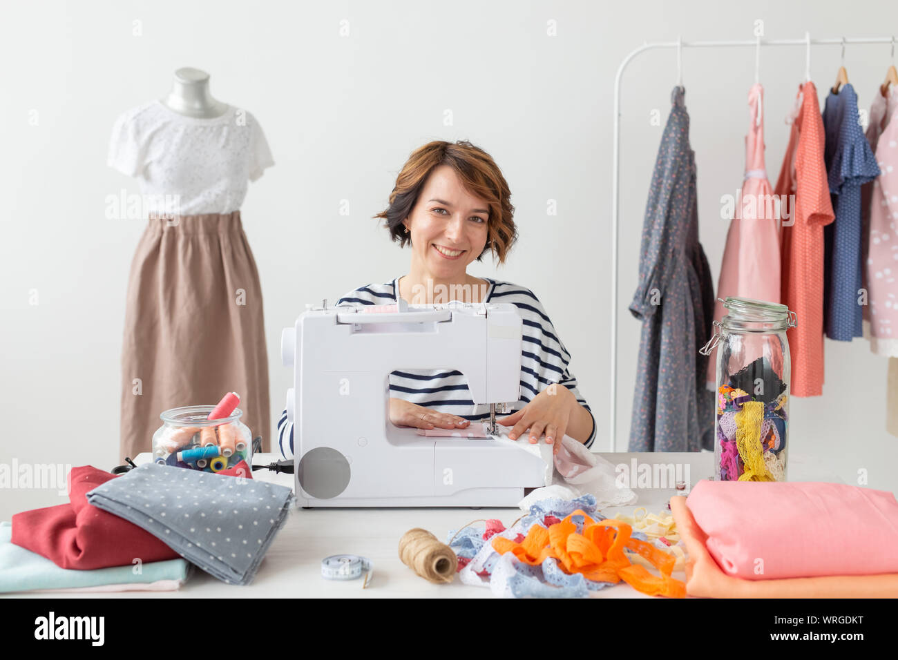 Young seamstress woman sews a new product on a sewing machine sitting ...