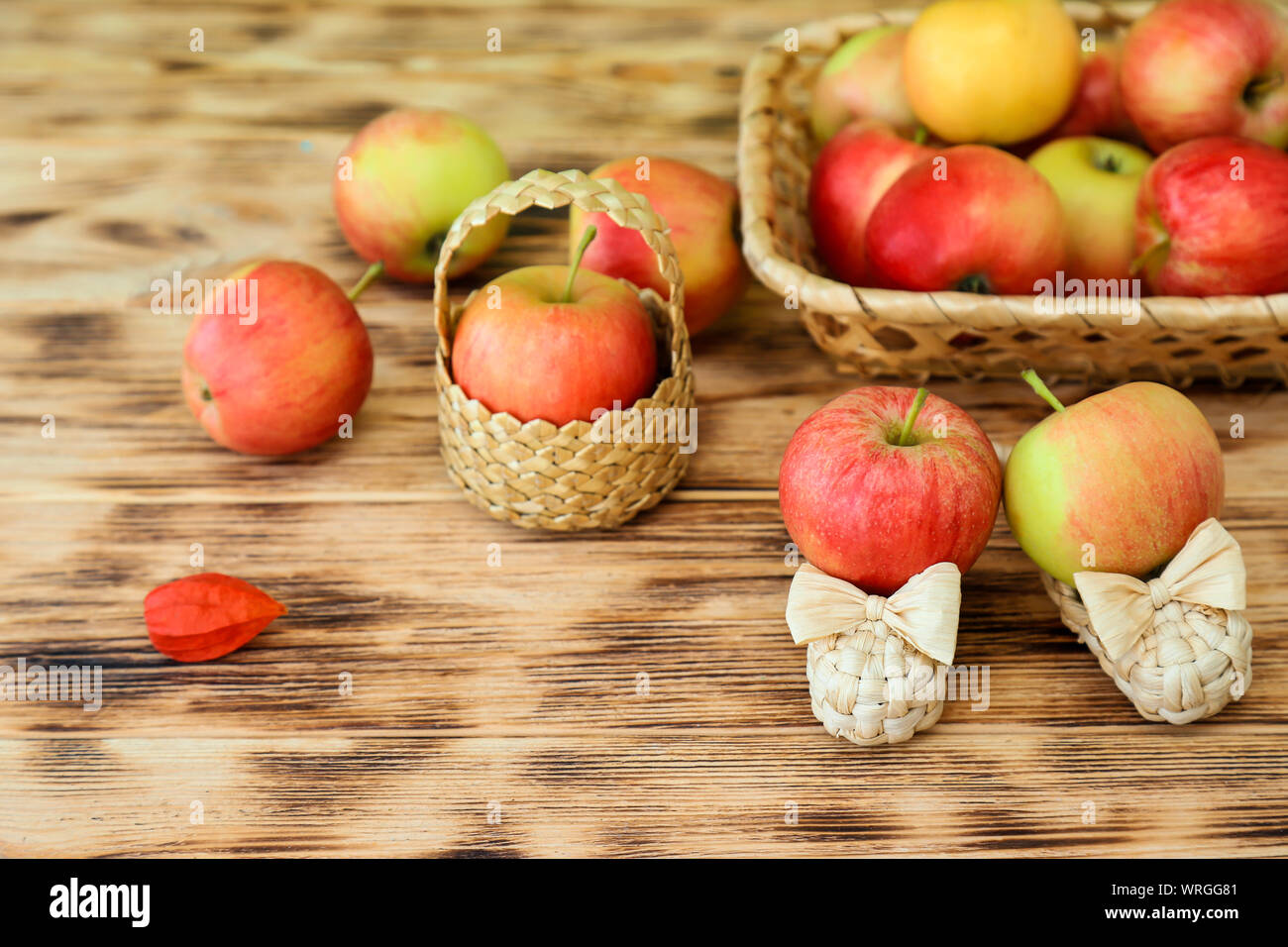 Red apples lie in a wicker plate on a wooden table. Wicker shoes and ...