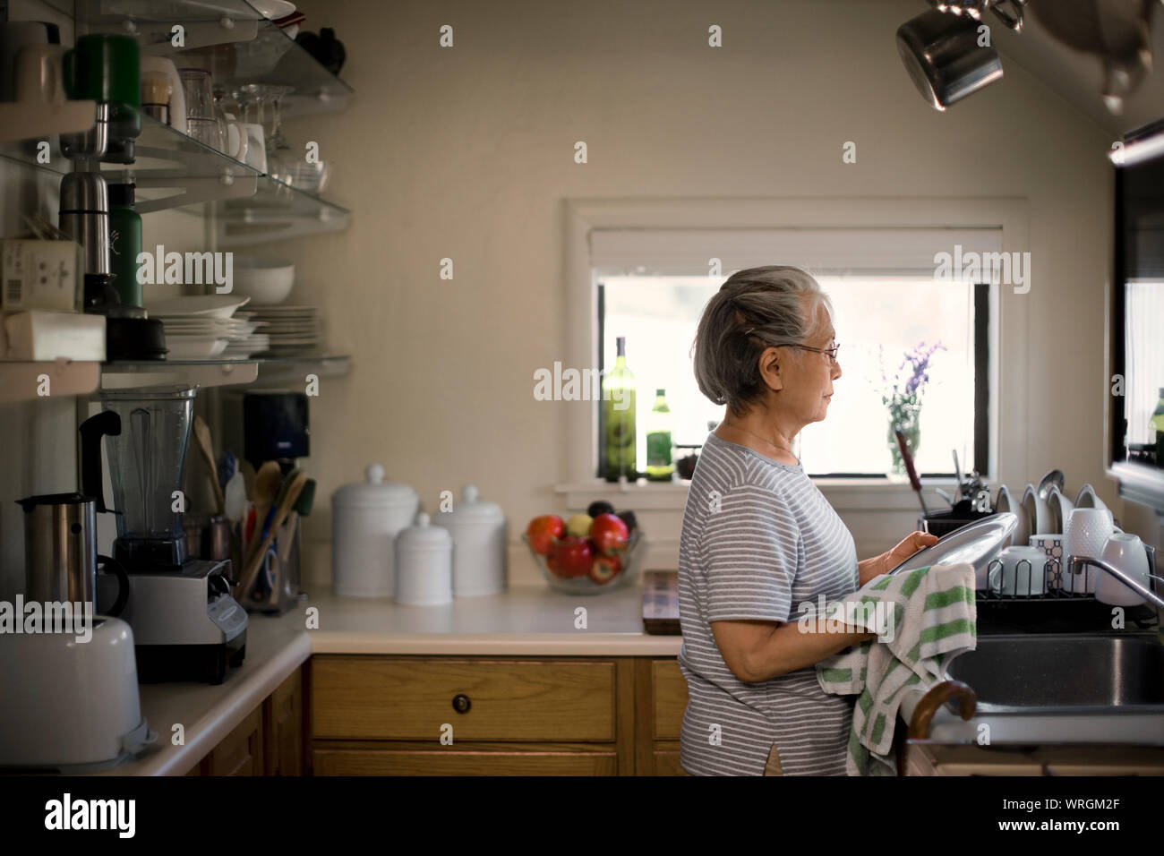 Contemplative senior woman washing dishes. Stock Photo