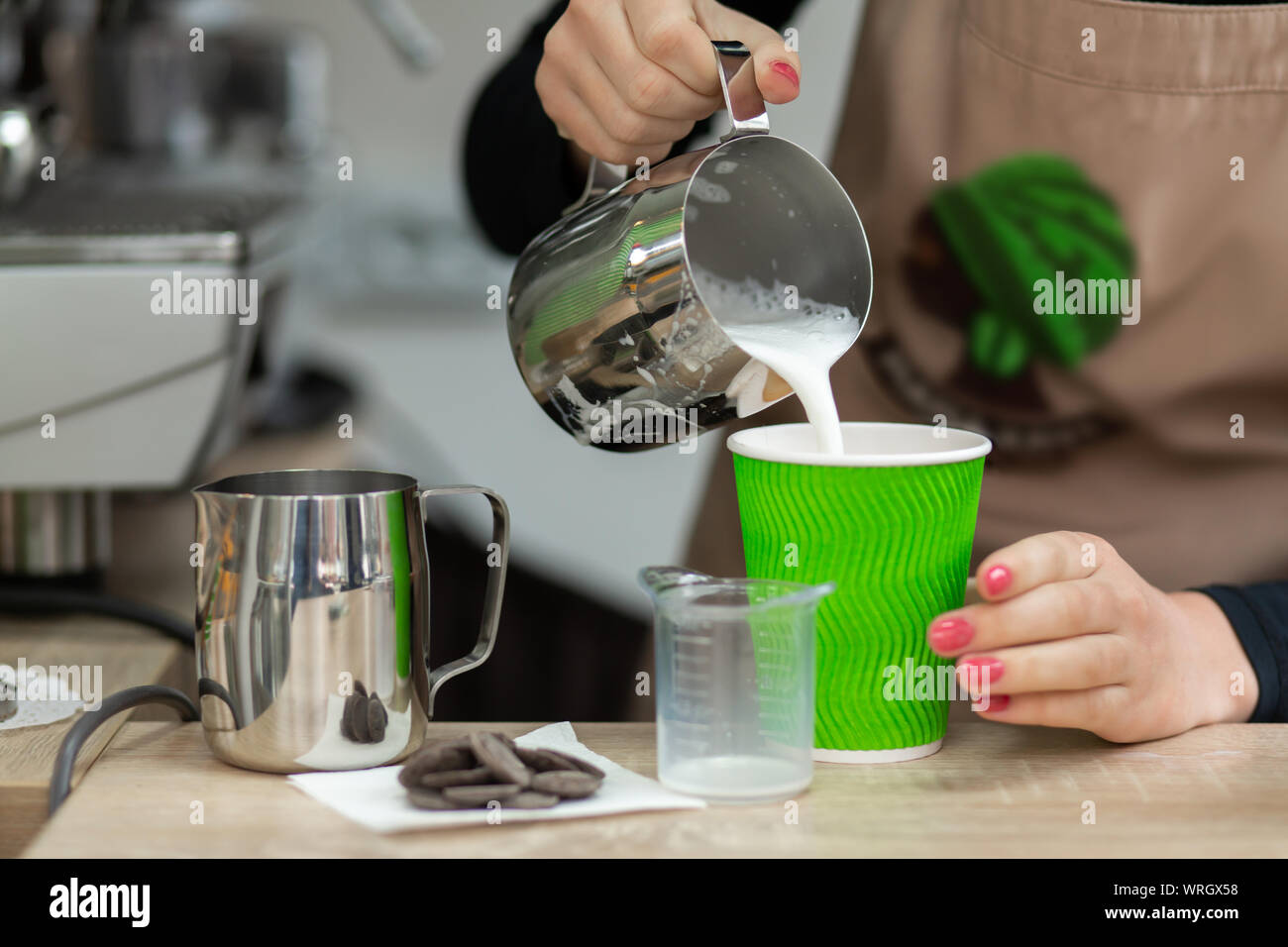 Barista in an apron pours milk into a green eco-friendly paper cup ...