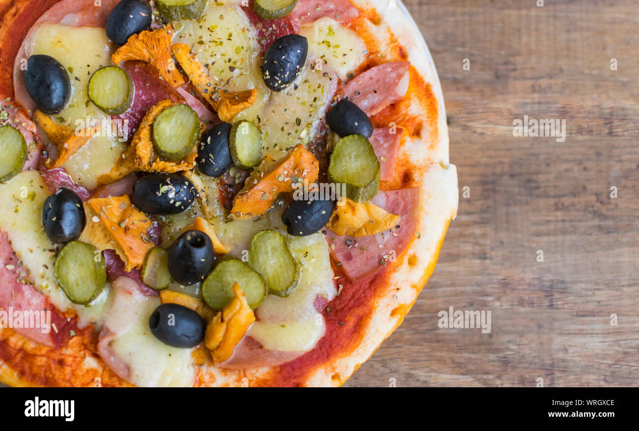 Homemade pizza with tomato sauce, cheese , olives , ham and mushrooms on wooden table. High angle view with space for text Stock Photo