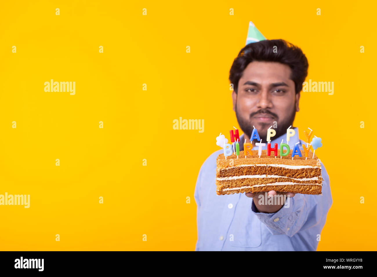 Crazy cheerful young indian man in paper congratulatory hat holding cakes  happy birthday standing on a yellow background. Jubilee congratulations  conc Stock Photo - Alamy