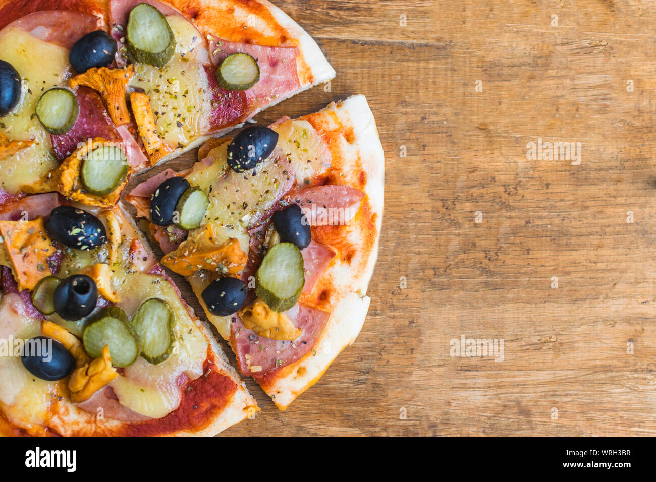 Homemade pizza with tomato sauce, cheese , olives , ham and mushrooms on wooden table. High angle view with space for text Stock Photo